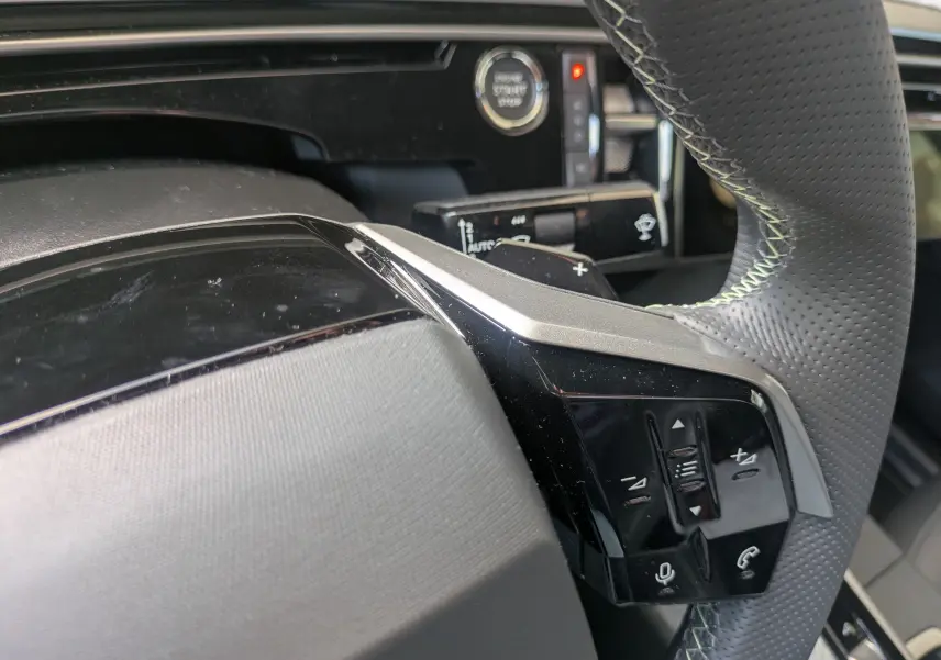 Gros plan sur le volant noir perforé avec commandes intégrées et surpiqûres vert clair du Peugeot 3008 Hybrid 2025.