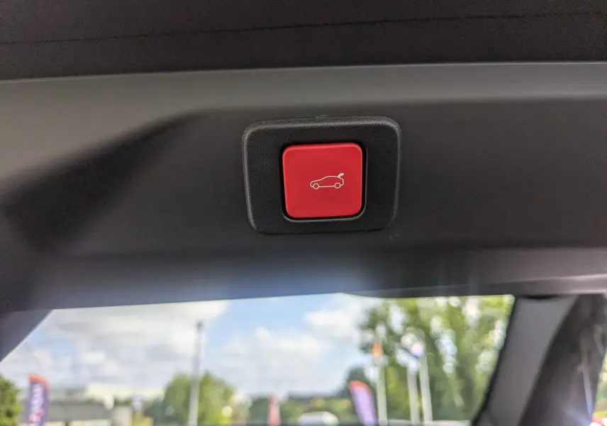 Bouton rouge d'ouverture électrique du hayon visible à l'intérieur du coffre du Peugeot 3008 noir 2025.