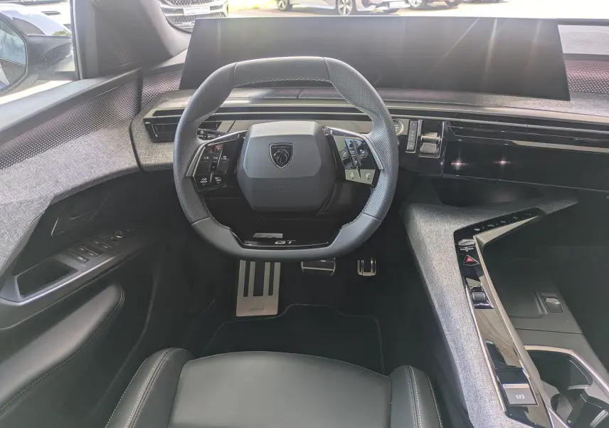 Vue intérieure centrée sur le volant compact noir et gris du Peugeot 3008 Hybrid 145 GT avec tableau de bord moderne et tissu gris.