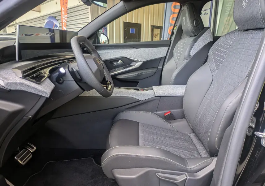 Intérieur côté conducteur du Peugeot 3008 Hybrid 145 GT 2025, sellerie tissu gris avec surpiqûres Iced Clay et tableau de bord moderne.