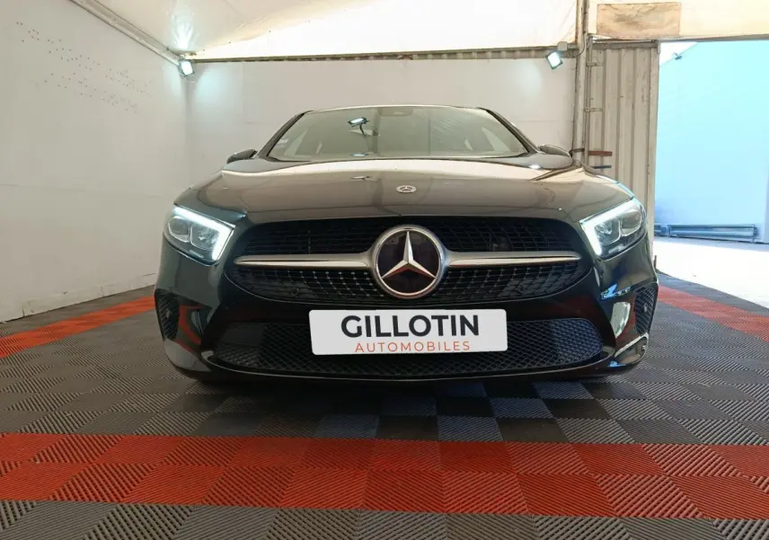 Vue frontale d'une Mercedes Classe A noire 2022 avec phares LED allumés dans un garage éclairé.