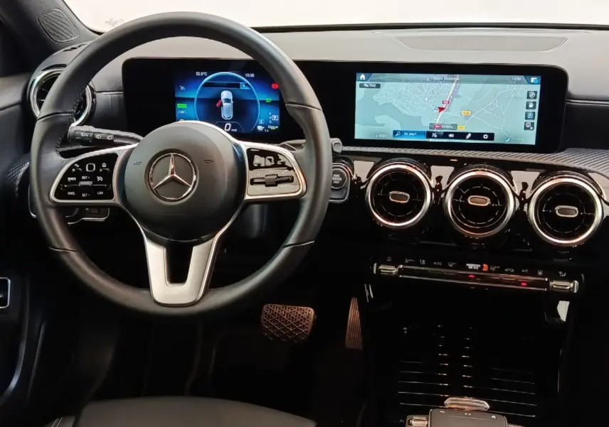 Vue intérieure centrée sur le volant cuir noir et le tableau de bord avec écran tactile et navigation 3D de la Mercedes Classe A.
