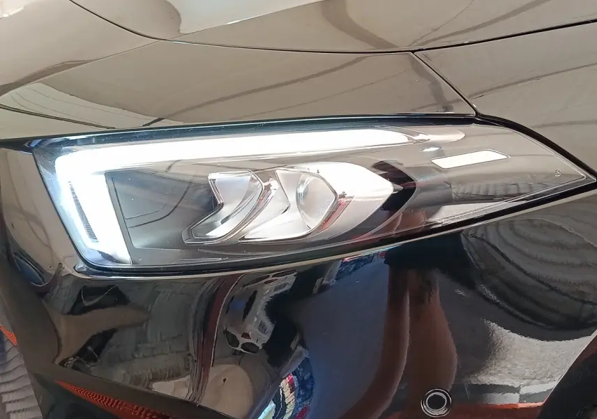 Gros plan sur le phare avant droit allumé d’une Mercedes Classe A 250 e Business Line noire, reflet brillant sur la carrosserie.