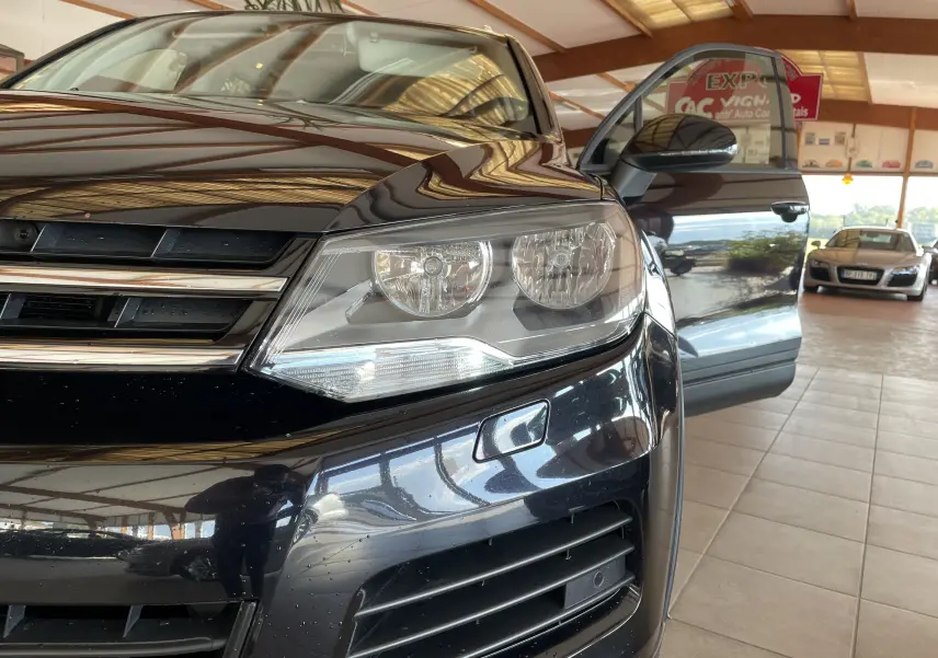 Gros plan sur l'avant droit noir brillant d'un Volkswagen Touareg 2012 avec porte ouverte dans un showroom.