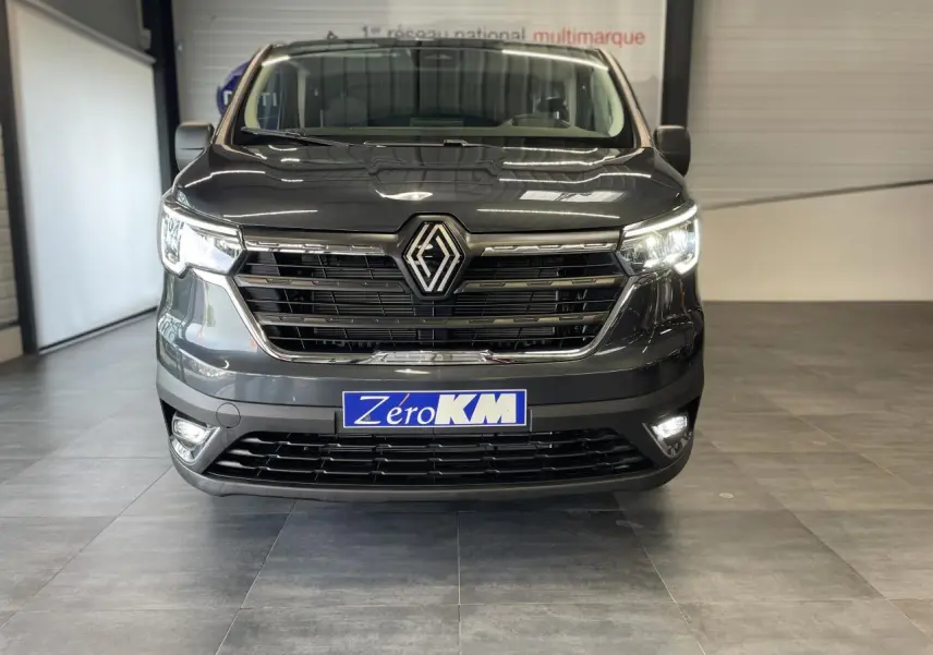Vue frontale du Renault Trafic Fourgon gris Comète 2025 avec phares Full LED allumés en intérieur showroom.