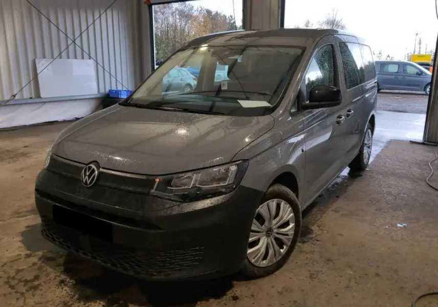 Vue 3/4 avant droit du Volkswagen Caddy Maxi gris Pure Grey, avec pare-chocs noir et jantes acier en intérieur d'atelier.