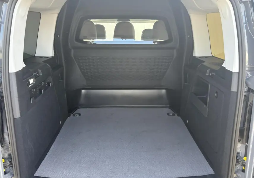 Vue intérieure arrière du coffre spacieux du Volkswagen Caddy Pure Grey 2024, montrant la cloison de séparation et les finitions noires.