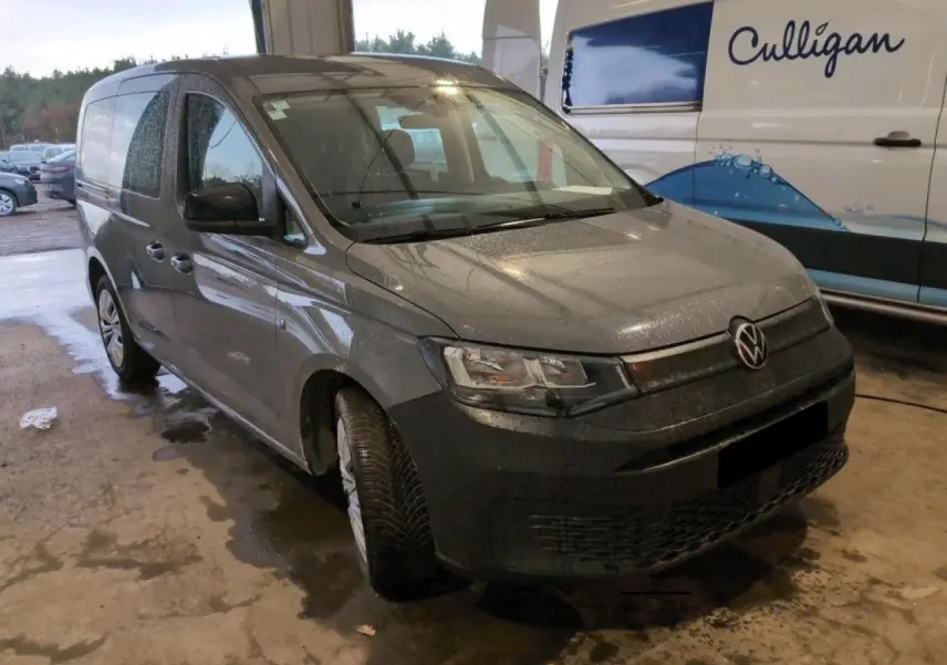 Vue 3/4 avant gauche d'un Volkswagen Caddy Maxi 2024 gris Pure Grey avec portes latérales coulissantes, stationné en intérieur.