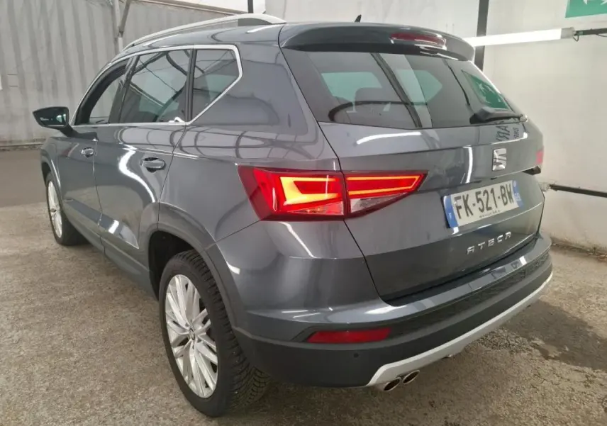 Vue 3/4 arrière droite d'un SEAT Ateca gris clair avec feux arrière LED allumés et double sortie d'échappement chromée.