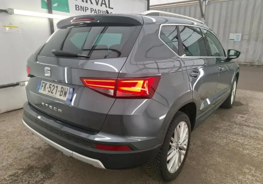 Vue 3/4 arrière droite d'un SEAT Ateca gris clair avec feux arrière LED allumés et jantes alliage 18 pouces.