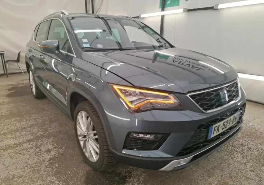 Vue 3/4 avant droit d'un SEAT Ateca gris clair avec phares LED allumés dans un garage intérieur.
