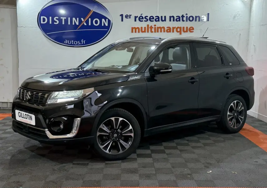 Suzuki Vitara noir en vue 3/4 avant droit, avec jantes alliage et calandre chromée brillante.