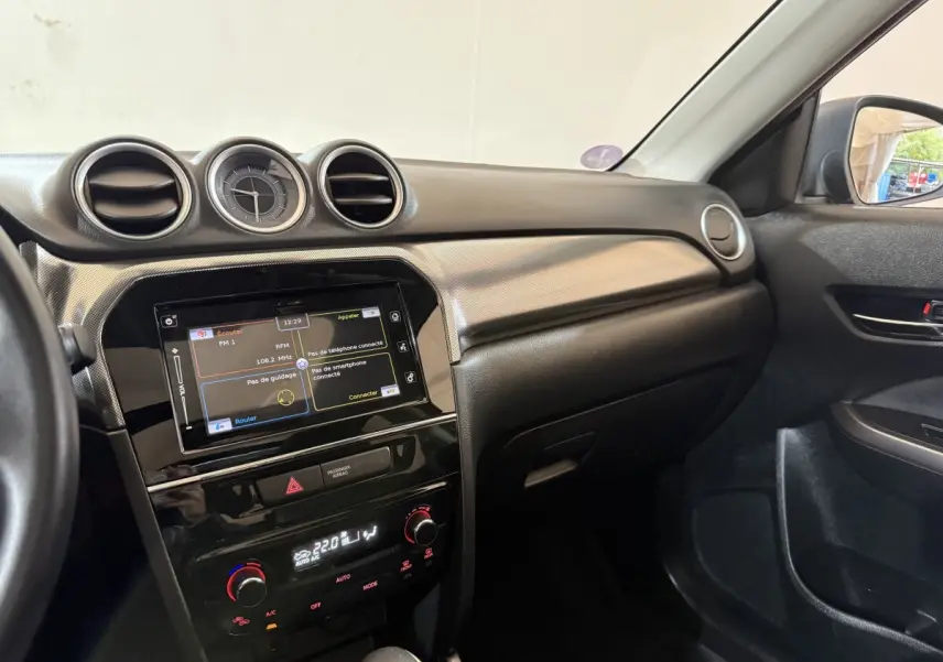 Vue intérieure côté passager du tableau de bord noir du Suzuki Vitara 2022 avec écran tactile et horloge centrale.