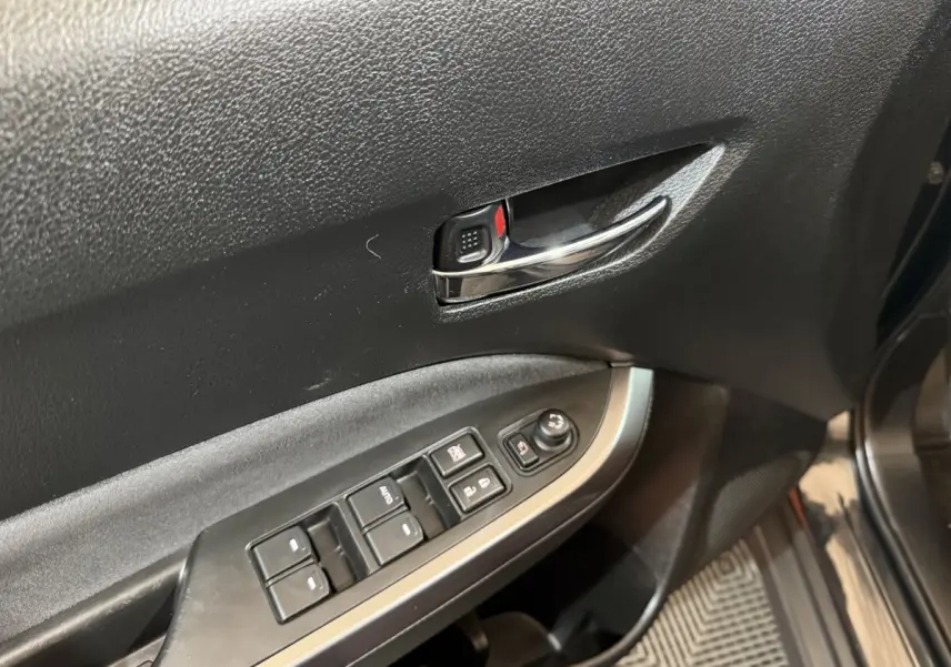 Gros plan sur la porte avant gauche du Suzuki Vitara noir, montrant la poignée chromée et les commandes des vitres électriques.
