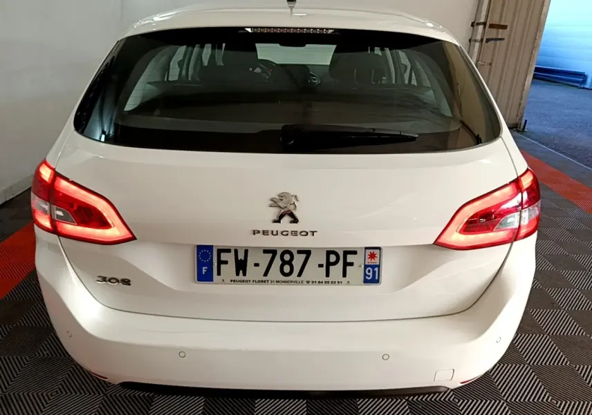 Vue arrière d’une Peugeot 308 blanche avec feux allumés et plaque d’immatriculation française visible.