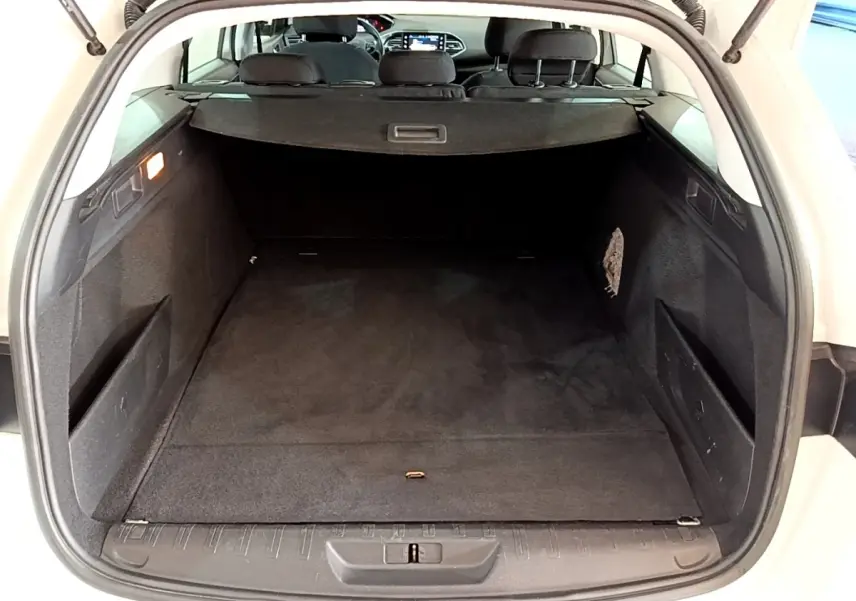 Vue arrière du coffre ouvert d'une Peugeot 308 blanche, montrant l'espace de chargement et la tablette cache-bagages noire.