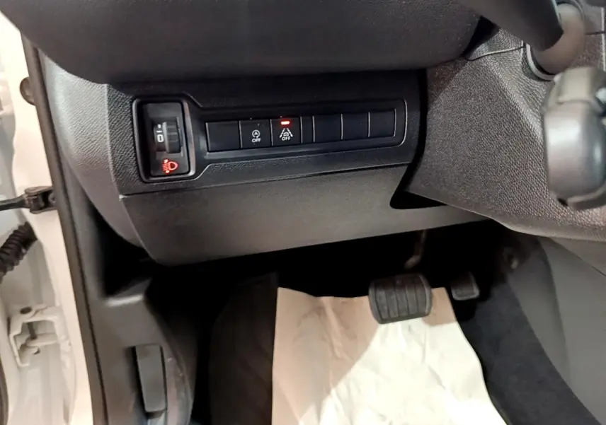 Vue intérieure côté conducteur montrant les commandes d'éclairage et d'assistance sur fond noir, Peugeot 308 blanc visible à l'ouverture.
