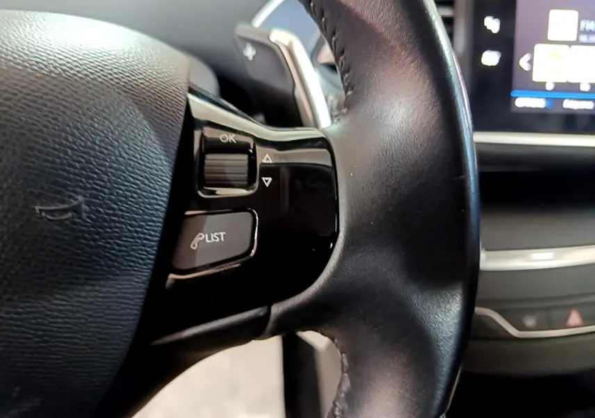Gros plan sur le volant cuir noir de la Peugeot 308 avec commandes multifonctions et écran tactile partiellement visible.