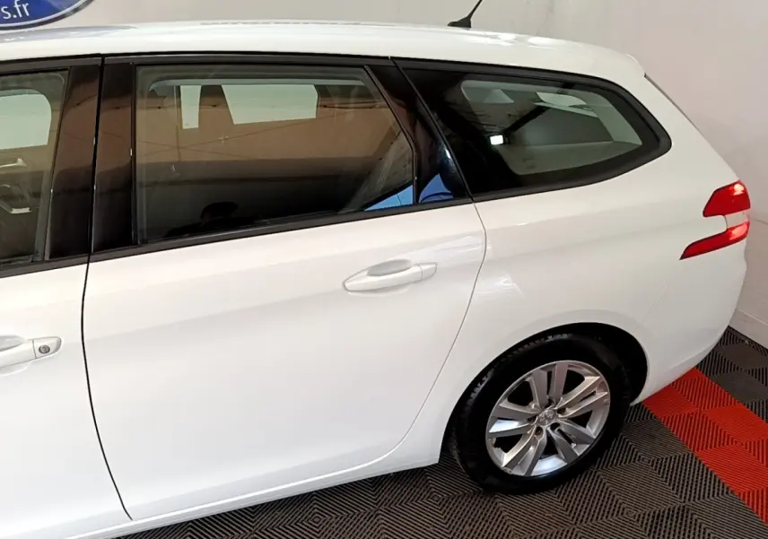 Vue latérale droite d'une Peugeot 308 break blanche, mettant en valeur la porte arrière et la roue arrière.