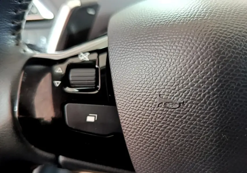Gros plan sur le volant en cuir noir de la Peugeot 308, avec commandes intégrées et bouton de klaxon visible.