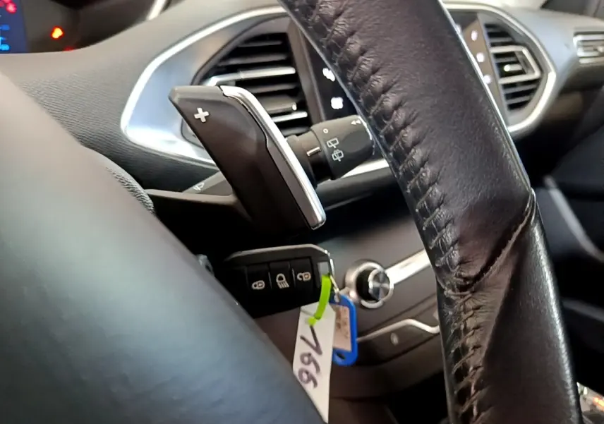 Gros plan intérieur sur le volant cuir noir et la commande de boîte auto de la Peugeot 308 blanche, avec clé et tableau de bord partiel.