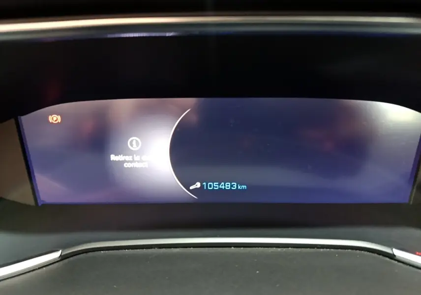 Tableau de bord numérique de Peugeot 308 blanc, affichant 105483 km et un message d'alerte clé.