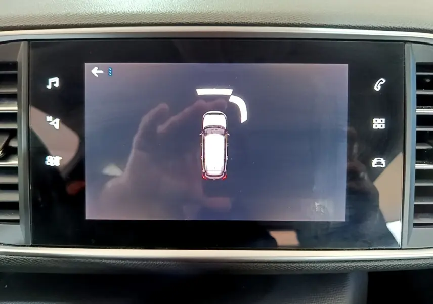 Écran tactile central montrant l’alerte de proximité arrière d’une Peugeot 308 blanche, vue intérieure.
