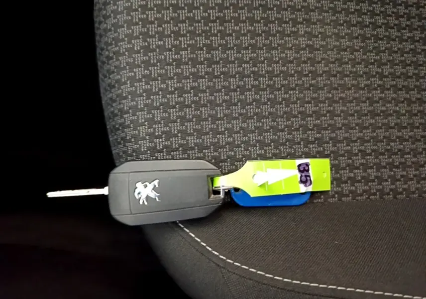 Gros plan sur la clé noire Peugeot posée sur un siège tissu gris à motifs avec étiquette verte numérotée 35.