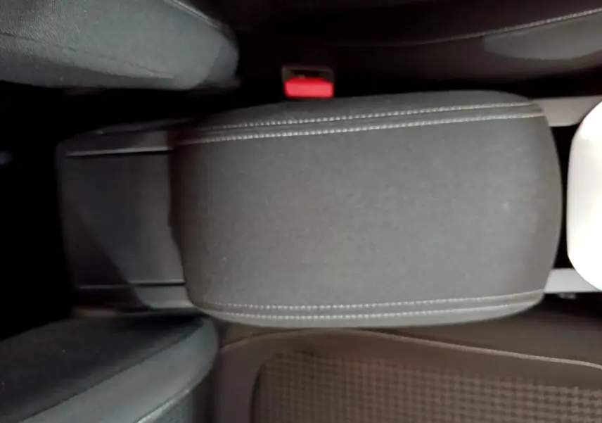 Vue rapprochée de l'accoudoir central noir et des sièges avant tissu dans l'habitacle d'une Peugeot 308 blanche.