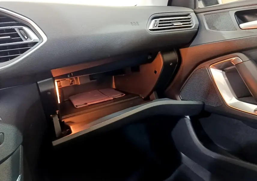 Vue intérieure côté passager de la Peugeot 308 blanche, boîte à gants ouverte avec éclairage intérieur visible.