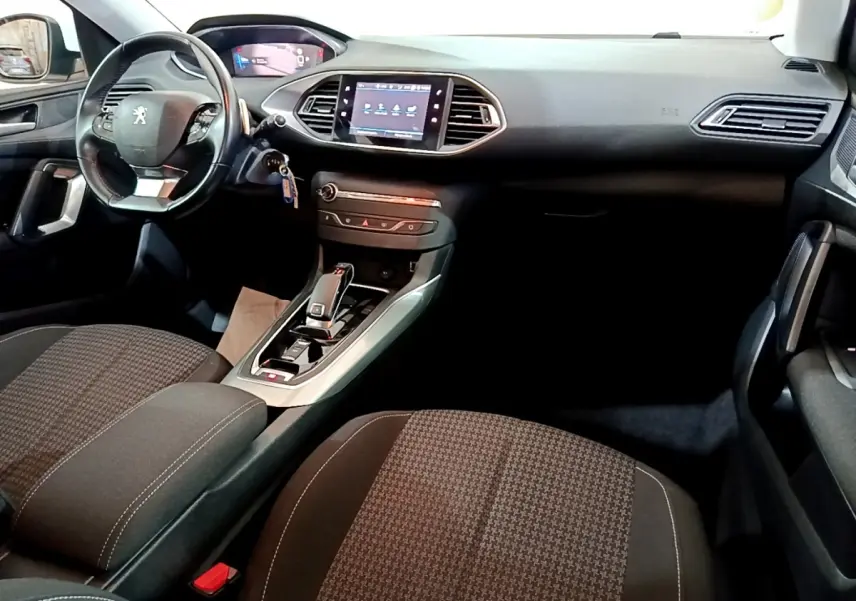 Vue intérieure avant de la Peugeot 308 blanche, montrant le tableau de bord, volant cuir multifonctions et écran tactile central.