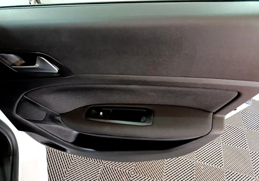 Vue rapprochée de la porte intérieure côté gauche de la Peugeot 308 blanche, avec poignée et commande de vitre noire.