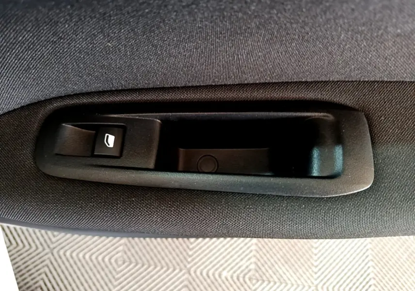 Gros plan sur la poignée intérieure noire avec bouton de lève-vitre sur la porte arrière d’une Peugeot 308 blanche.