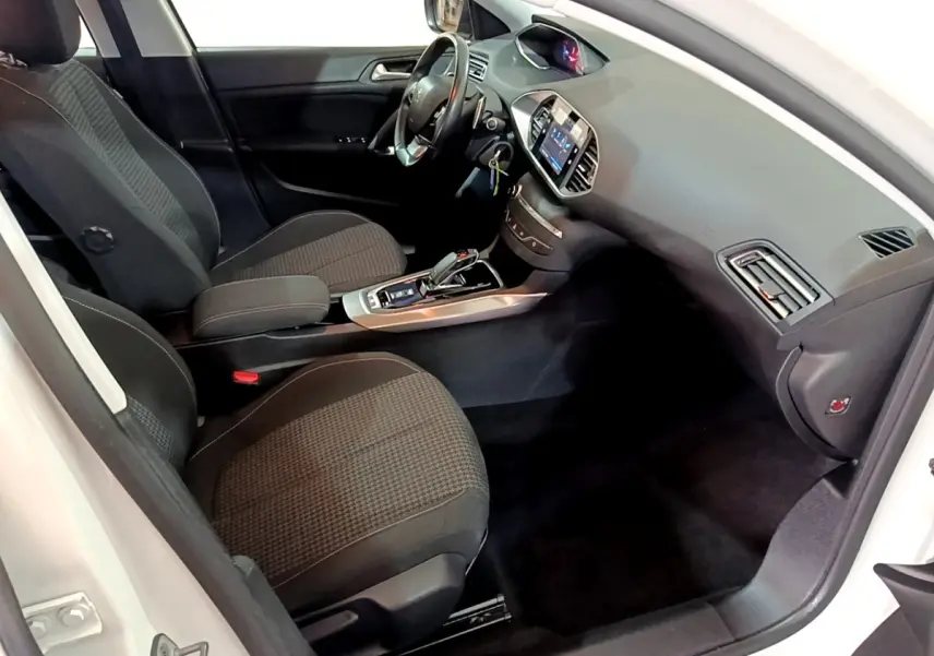 Vue intérieure côté conducteur de la Peugeot 308 blanche, montrant sièges noirs, volant cuir et tableau de bord digital.