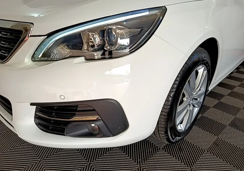 Gros plan sur l'avant droit blanc d'une Peugeot 308 2021, mettant en valeur le phare LED et la roue alliage.