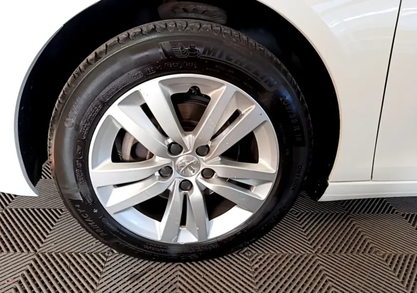 Gros plan sur la roue avant gauche d’une Peugeot 308 blanche, jante alliage et pneu Michelin visibles.