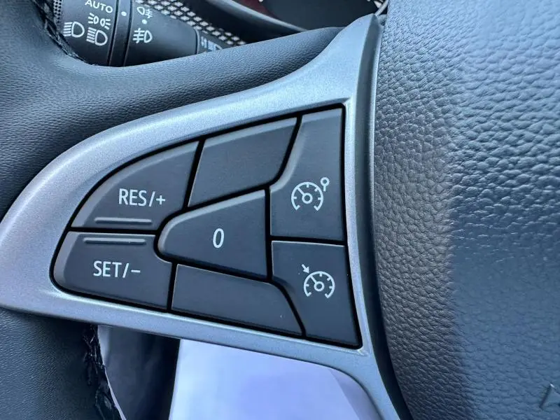 Gros plan sur les commandes de régulateur de vitesse au volant noir de la Dacia Sandero beige Safari.