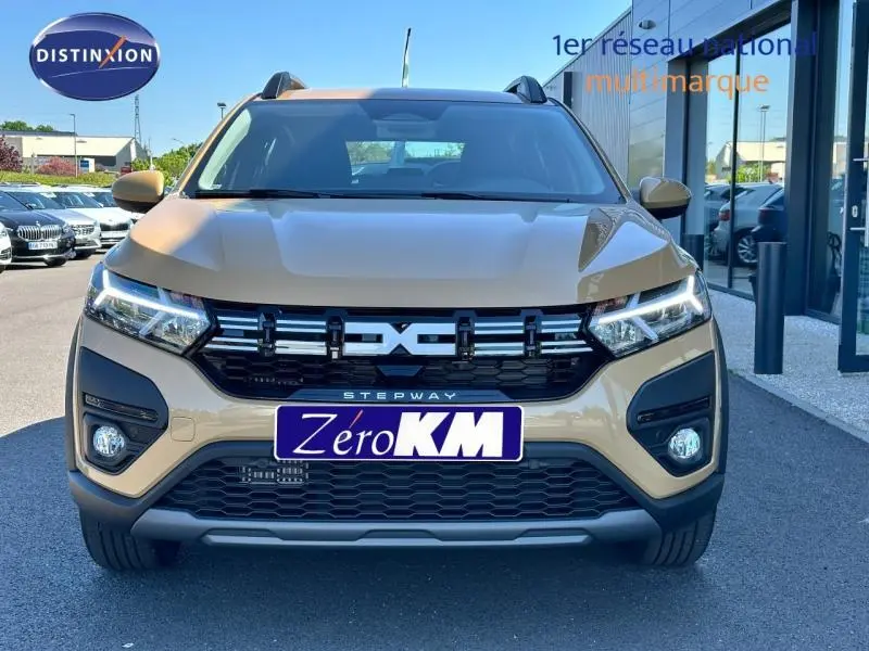 Vue avant d'une Dacia Sandero Stepway beige Safari avec calandre noire et phares LED allumés.