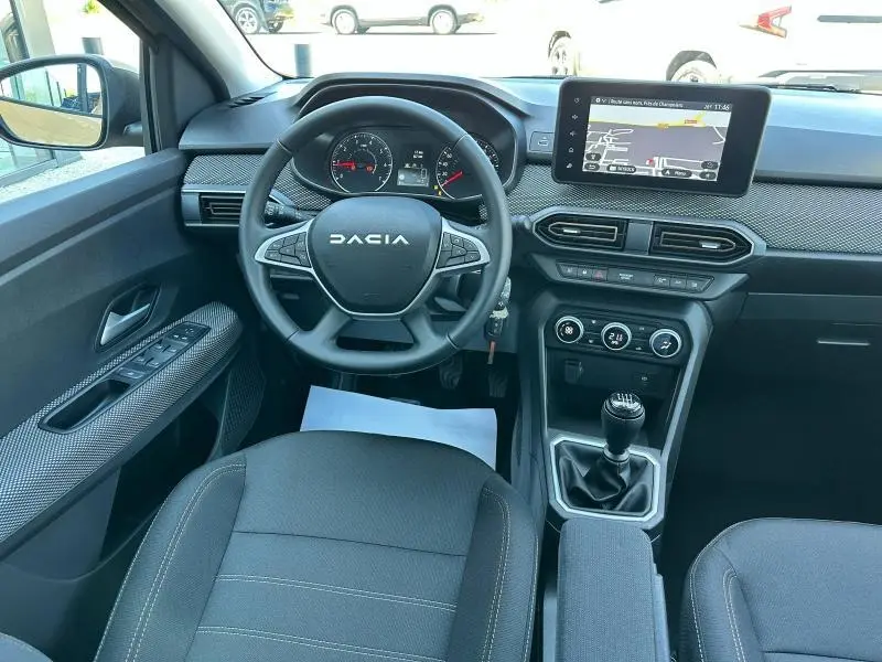 Vue intérieure avant de la Dacia Sandero 2025, tableau de bord noir avec écran tactile et volant multifonction.