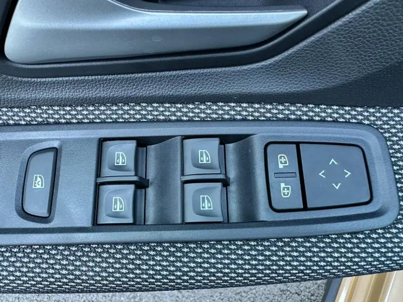 Gros plan sur les commandes de lève-vitres et réglage des rétroviseurs côté conducteur du Dacia Sandero beige Safari 2025.