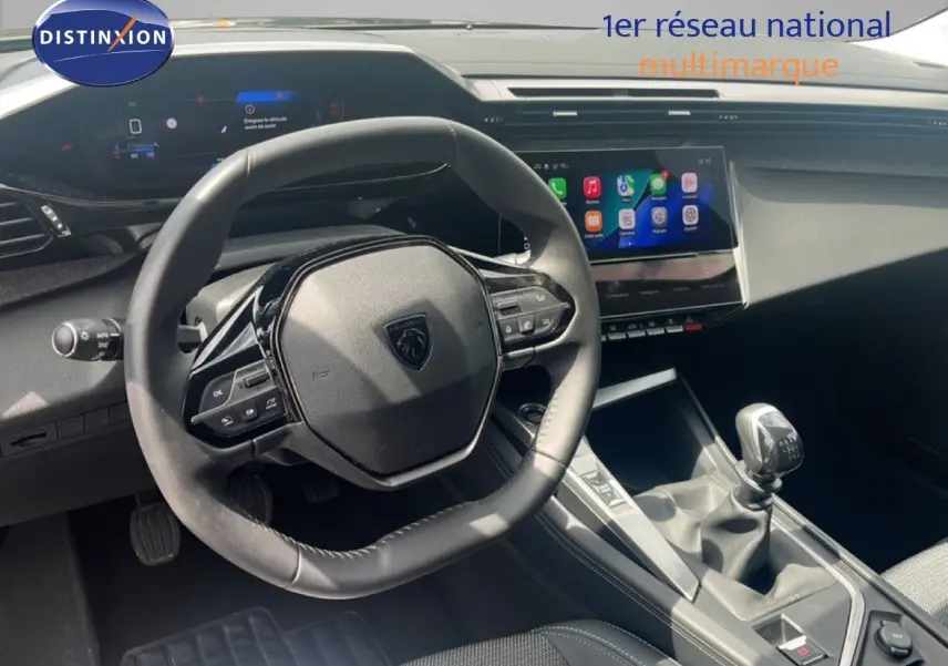 Vue intérieure centrée sur le volant et la console centrale d’une Peugeot 308 2024 avec boîte manuelle, ambiance noire moderne.