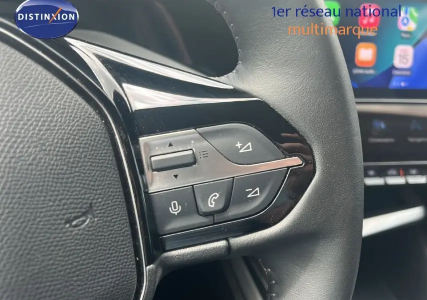 Gros plan sur les commandes au volant de la Peugeot 308 2024, finition Allure, avec cuir noir et écran tactile en arrière-plan.