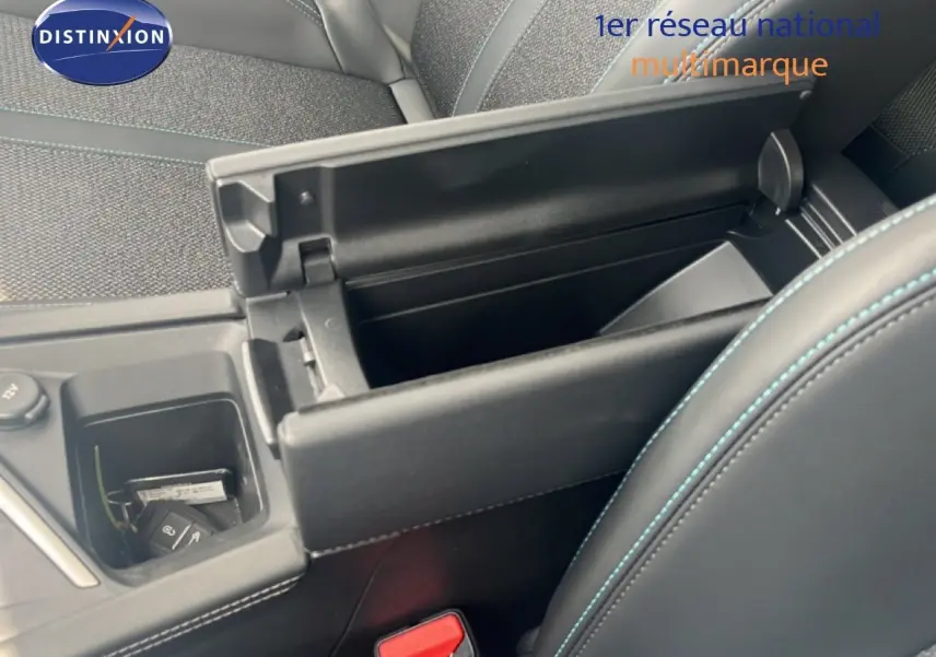 Vue intérieure rapprochée du coffre central ouvert et des sièges tissu gris noir avec surpiqûres bleues d’une Peugeot 308 2024.