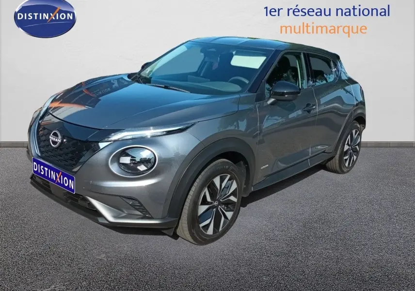 Nissan Juke Hybrid gris squale metal en 3/4 avant droit, avec jantes alliage et calandre noire distinctive.