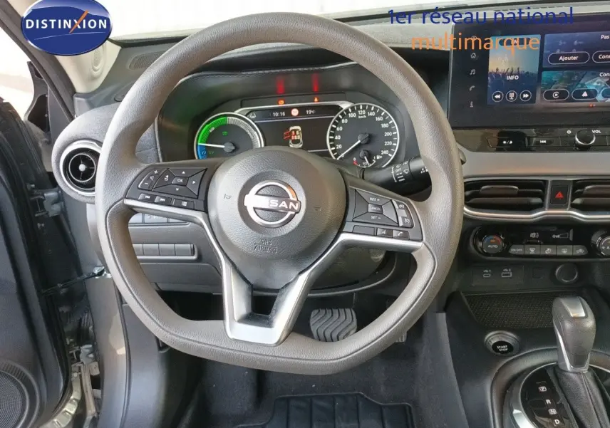 Vue intérieure centrée sur le volant et le tableau de bord du Nissan Juke Hybrid gris, avec écran tactile et commandes au volant.