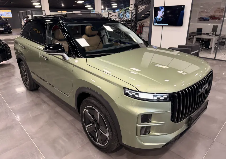 Vue 3/4 avant d’un SUV JAECOO J7 hybride rechargeable gris olive avec toit noir et intérieur cuir brun en showroom.