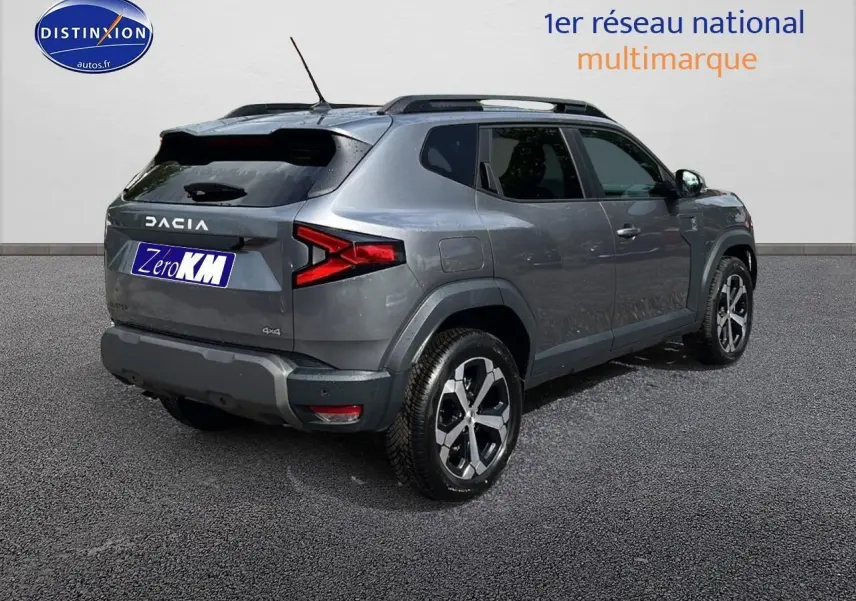 Vue 3/4 arrière droite du Dacia Duster gris schiste 2025 avec jantes alu et barres de toit visibles.