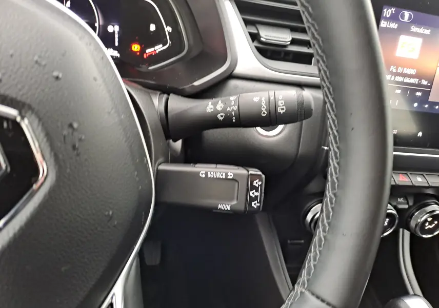 Vue intérieure du volant et des commandes du tableau de bord d'un Renault Captur gris Cassiopée, avec affichage numérique et boutons multifonctions.