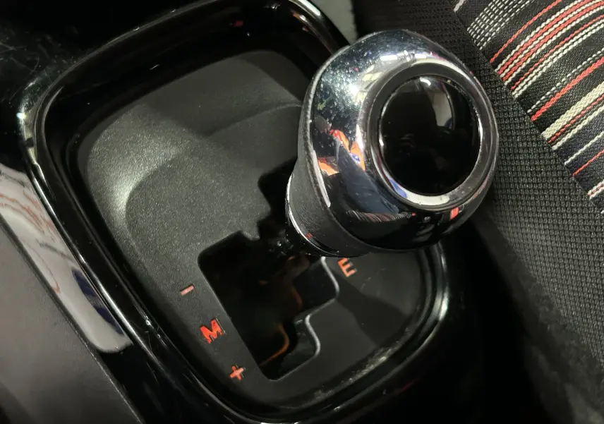 Gros plan sur le levier de vitesses automatique noir brillant de la Citroën C1 rouge, avec sièges tissu rayés visibles à droite.