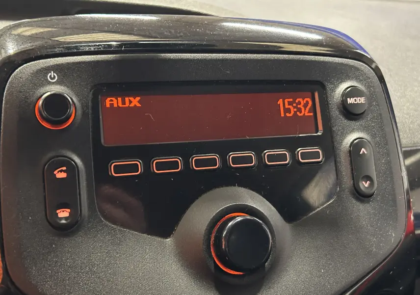 Gros plan sur l’autoradio noir de la Citroën C1 rouge, affichant l’heure 15:32 et la source AUX.